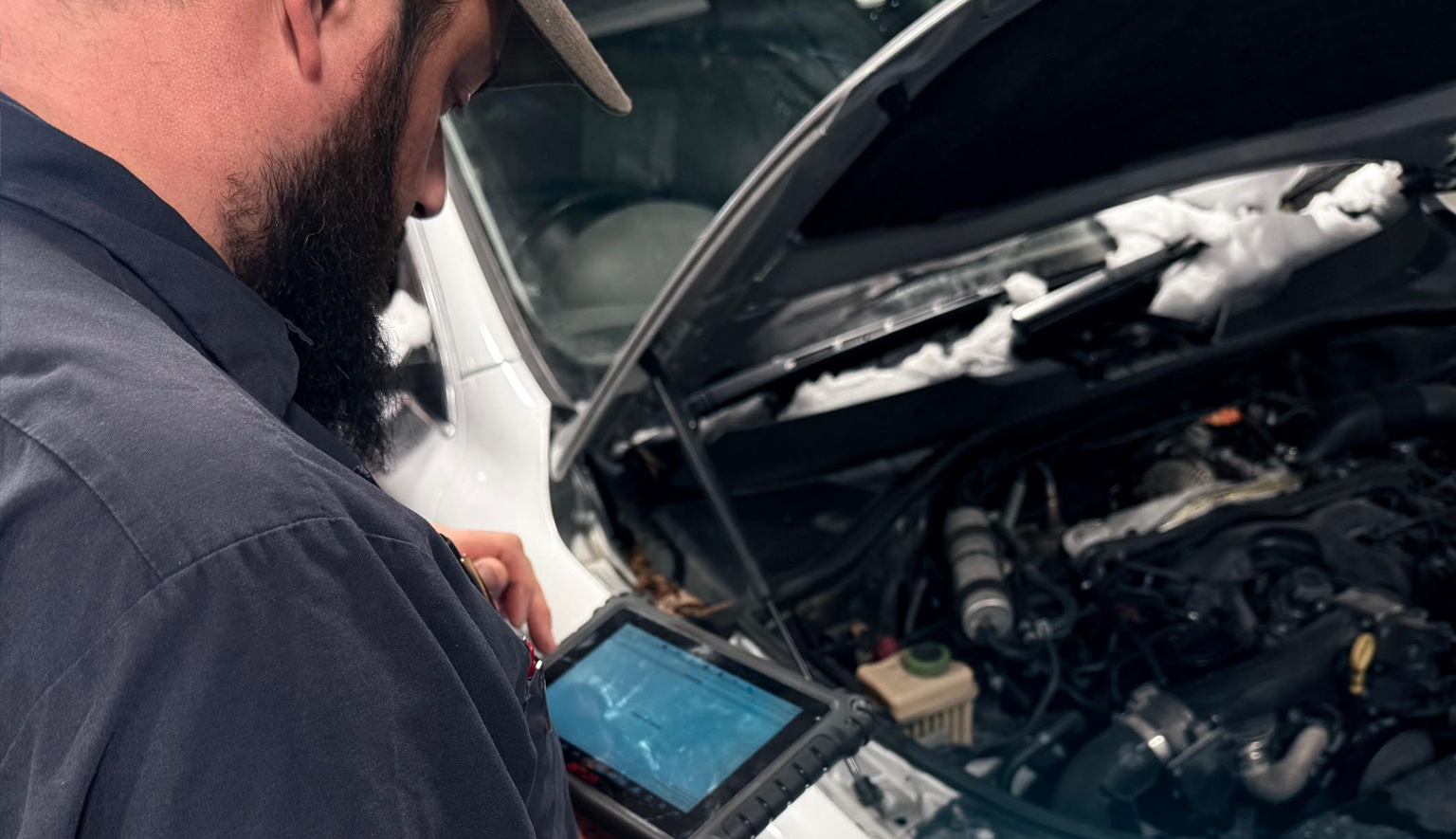 Technician performing full-system vehicle diagnostics with scan tool and testing equipment